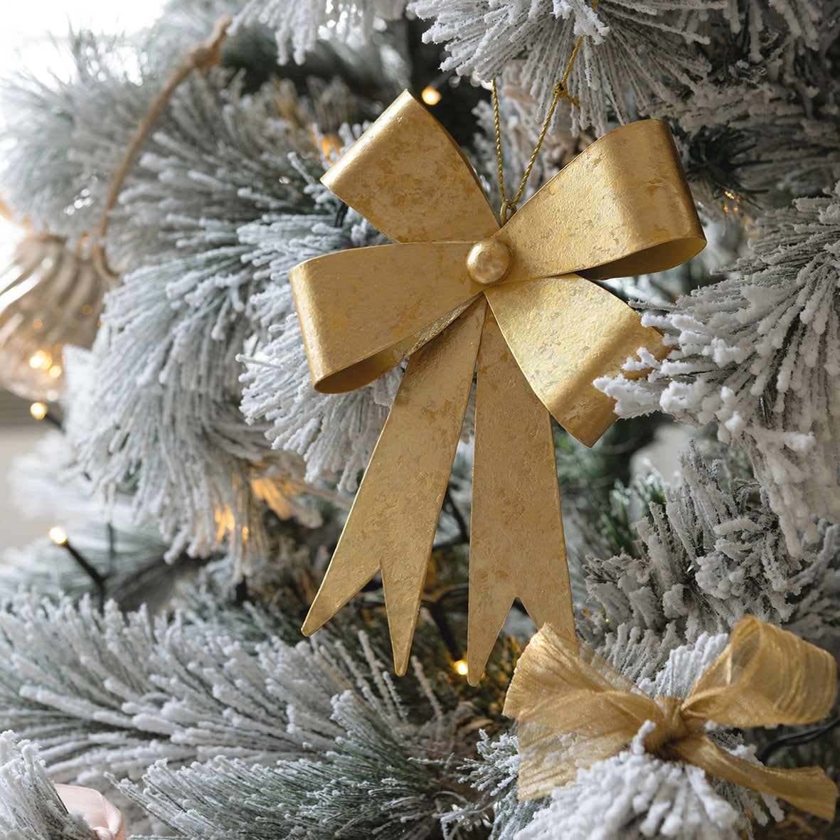 Photo mise en scène d'une décoration nœud métal doré suspendu à une branche du sapin de Noël.